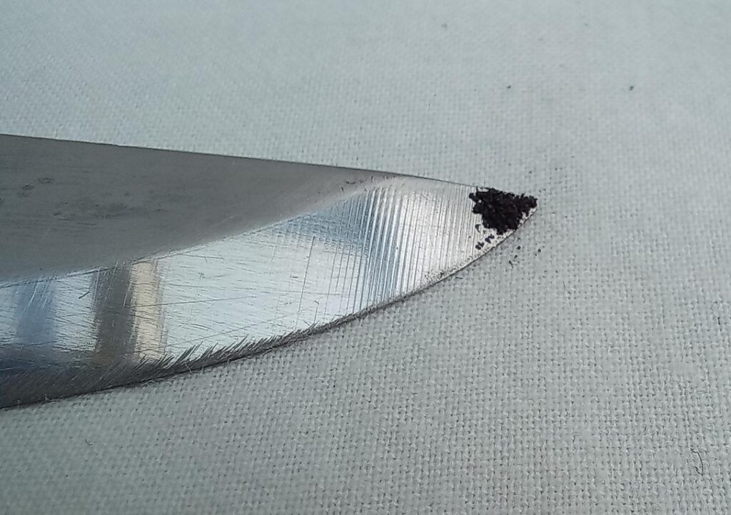 Flat layer of potassium permanganate  powder on a knife tip