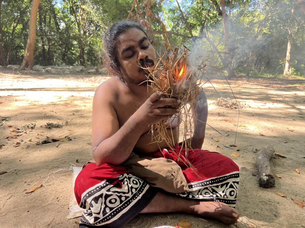 The grass bundle is catching fire from the Vedda flint and steel fire-making